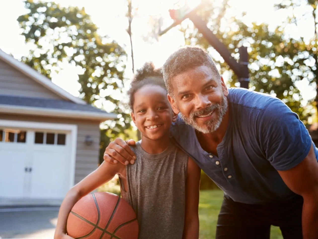 A man and girl holding a basketball in front of their home.