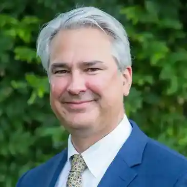 A man in a suit and tie standing next to a bush.