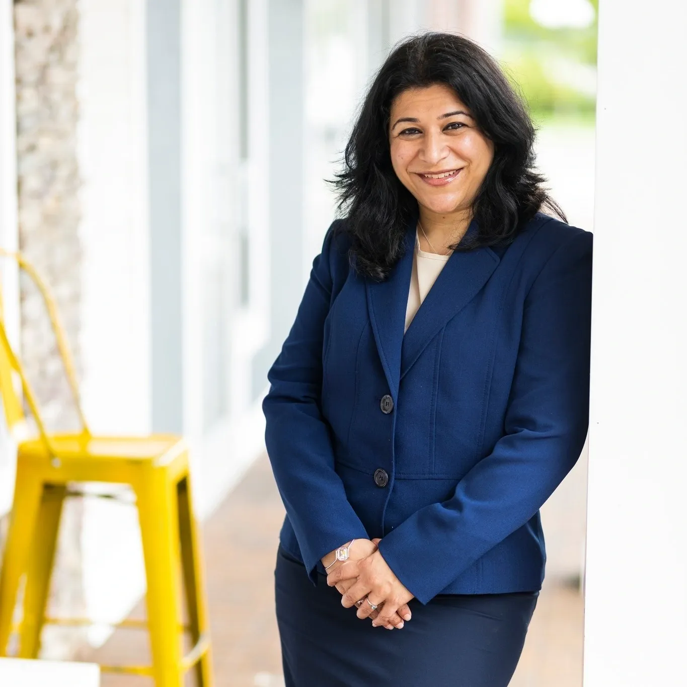 A woman in blue jacket standing next to yellow chair.