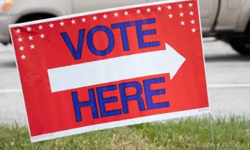 A red and white sign that says vote here.